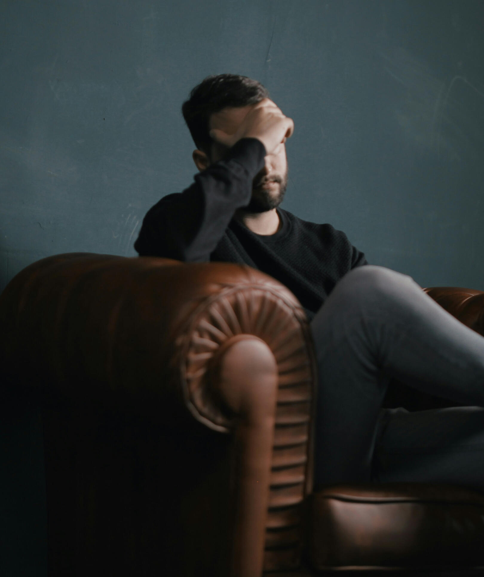 Photo of man holding his head while sitting on a sofa by Nik Shuliahin on Unsplash